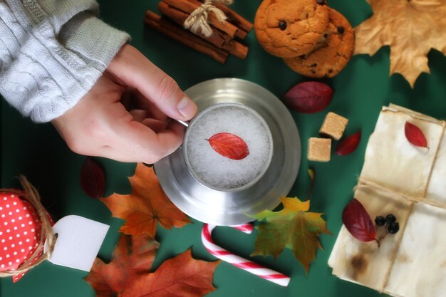 Manos sosteniendo una taza de café caliente sobre una mesa con hojas de otoño