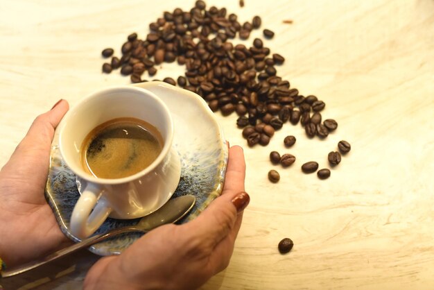 Manos sosteniendo una taza de café contra una mesa de madera y granos de café