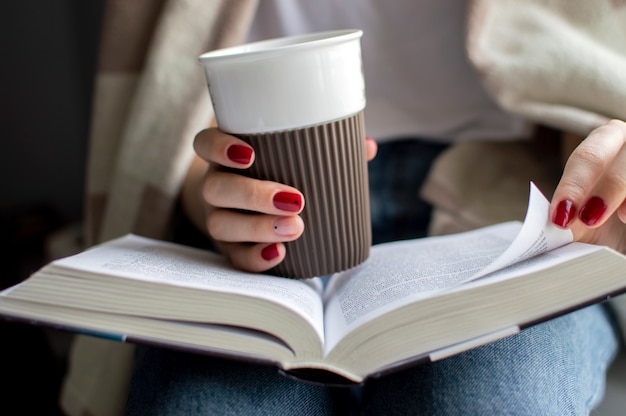 Manos sosteniendo una taza de café y un libro