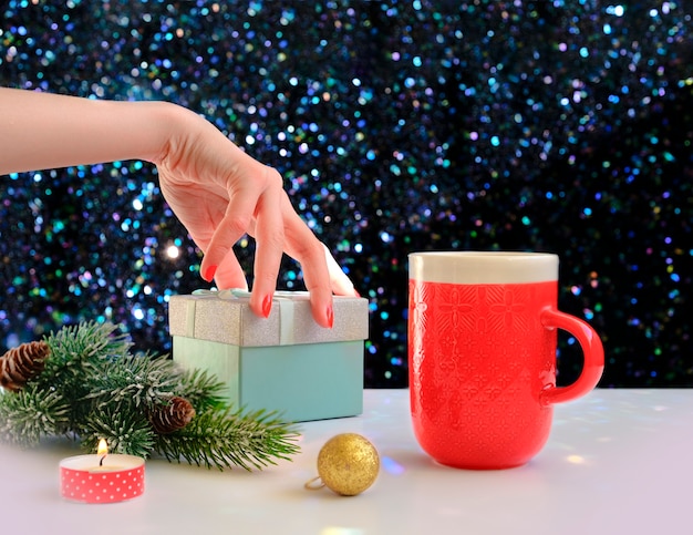 Manos sosteniendo una taza de café sobre un fondo de Navidad. Vista desde arriba. Manos femeninas sosteniendo la taza de café. Cajas de regalo de Navidad y abeto de nieve sobre mesa de madera.