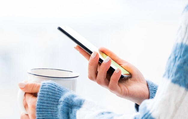 Manos sosteniendo la taza y el teléfono