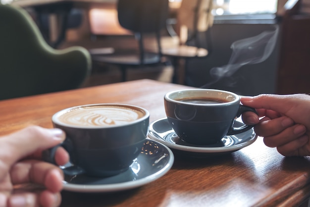 Manos sosteniendo tazas de café y chocolate caliente en la mesa de madera en la cafetería
