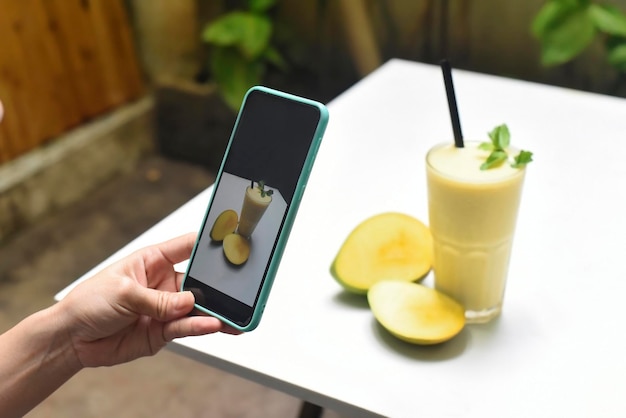 Manos sosteniendo un teléfono inteligente tomando una foto de batido de mango