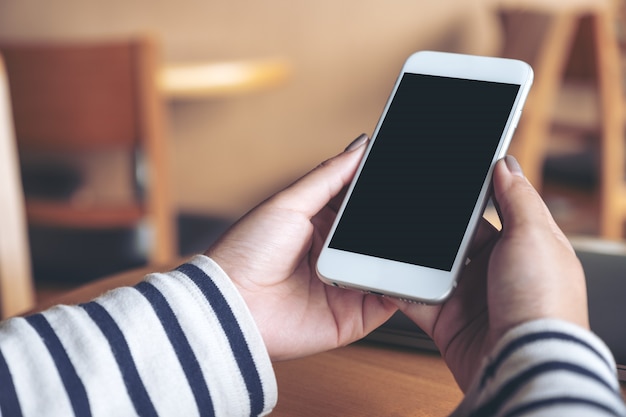 Manos sosteniendo teléfono móvil blanco con pantalla en blanco negro