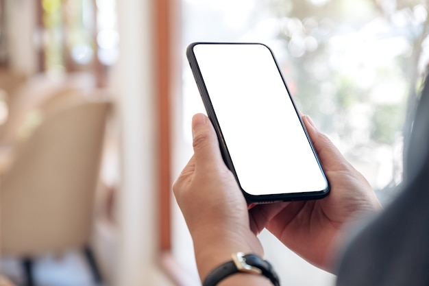 Manos sosteniendo un teléfono móvil negro con pantalla de escritorio en blanco en el café