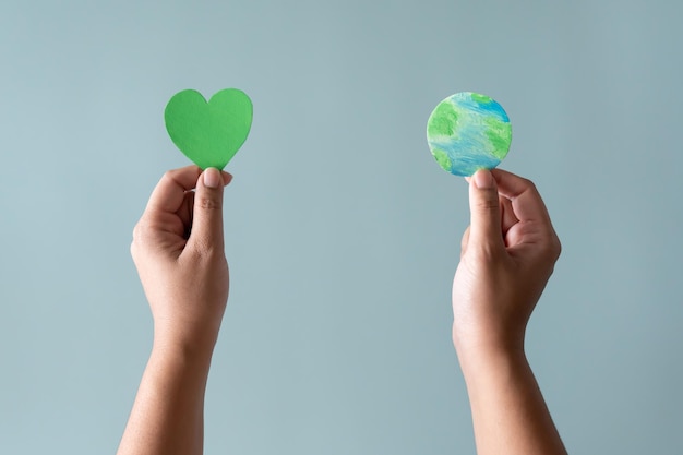 Manos sosteniendo la tierra y el concepto de forma de corazón verde de proteger al mundo del calentamiento global con ecoheart en mente