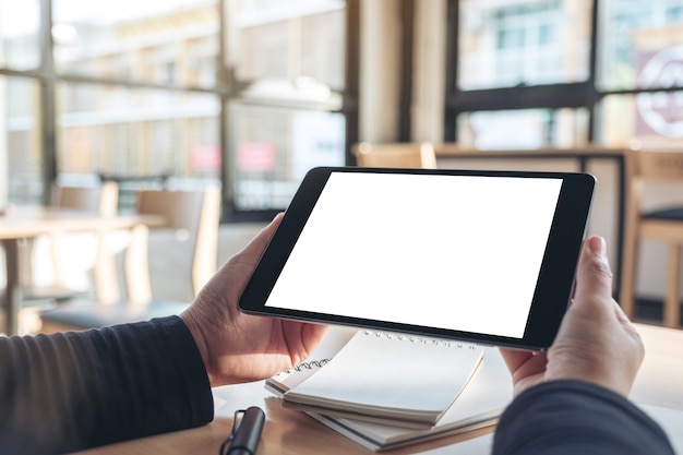 Manos sosteniendo y usando tablet pc negro con pantalla de escritorio en blanco mientras trabaja en portátiles en la oficina