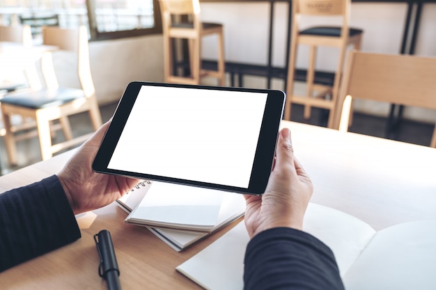 Manos sosteniendo y usando tableta negra con pantalla de escritorio blanca en blanco