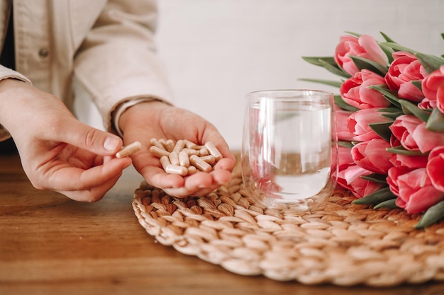 Manos sosteniendo vitaminas y un vaso de agua, atención médica y medicamentos.