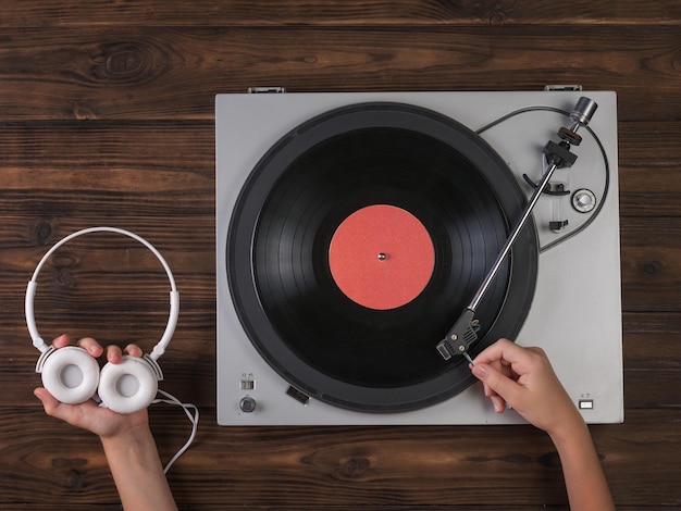 Las manos sostienen los auriculares blancos y colocan un disco de vinilo en el reproductor