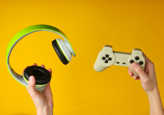 Manos sostienen auriculares estéreo y gamepad en superficie amarilla