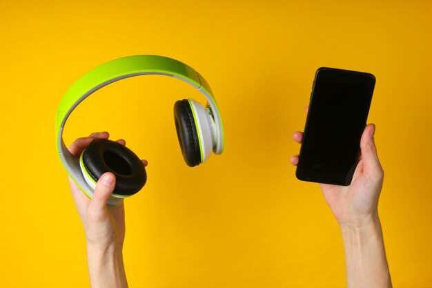 Manos sostienen auriculares estéreo y teléfono inteligente sobre una superficie amarilla