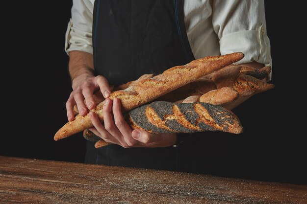 Manos sostienen baguettes recién horneadas contra el fondo negro de una mesa de madera