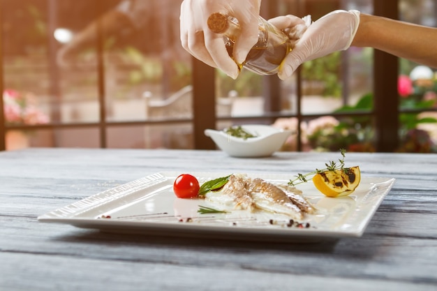 Las manos sostienen la botella sobre el pescado. Trozos de pescado con hierbas. Pescado dorado para el desayuno. Agrega un poco de aceite de oliva.