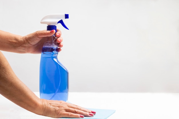 Las manos sostienen la botella de spray líquido azul y una esponja sobre la mesa. Copie el espacio. Productos de limpieza. Fondo blanco.