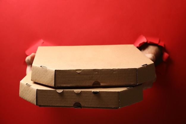 Foto manos sostienen cajas con sabrosa pizza en rojo