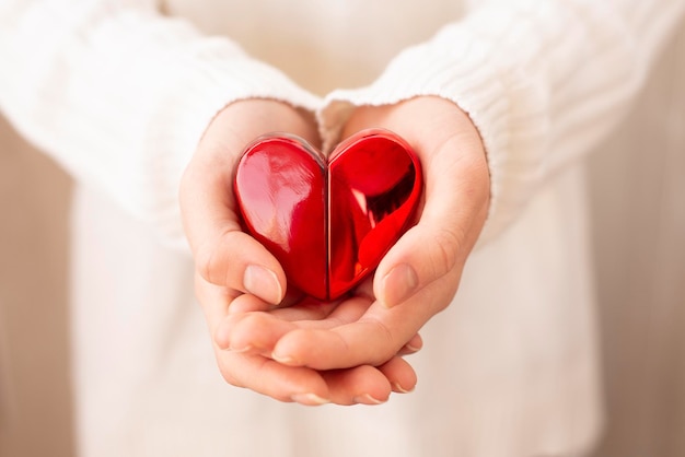 Las manos sostienen un corazón de recuerdo, un gesto de protección o cuidado, el concepto de mantener la salud, proteger las relaciones, los sentimientos y el amor. Enfoque selectivo. Símbolo de AMOR. Tarjeta del Día de San Valentín.