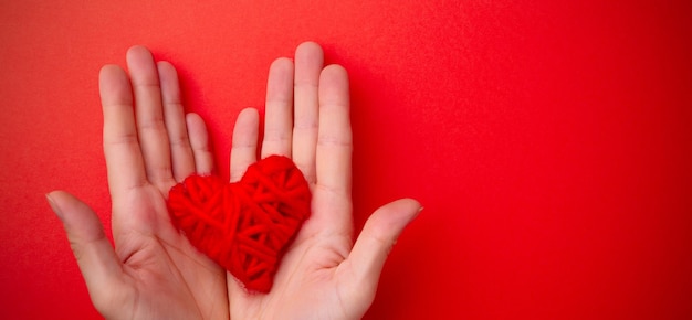 Manos sostienen corazón rojo sobre fondo rojo. Concepto del día de San Valentín