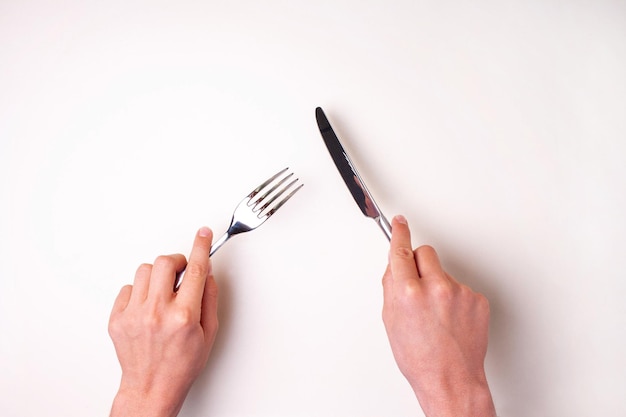Las manos sostienen un cuchillo con un tenedor sobre una mesa blanca aislada. Vista desde arriba