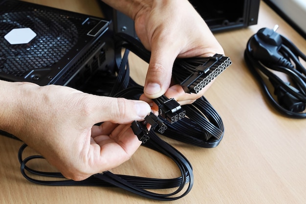 Las manos sostienen los enchufes para conectar la electricidad desde la unidad de fuente de alimentación a la placa base en la computadora