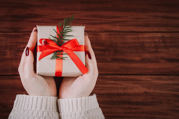 Las manos sostienen la hermosa caja de regalo sobre un fondo de madera. Tradición navideña.