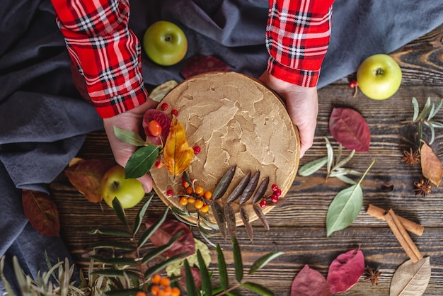 Las manos sostienen un pastel marrón mousse decorado con hojas de otoño y bayas