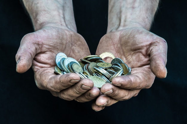 Foto manos sucias, pobre hombre sin hogar con muchas monedas de diferentes países que ilustran la pobreza en la sociedad del capitalismo moderno