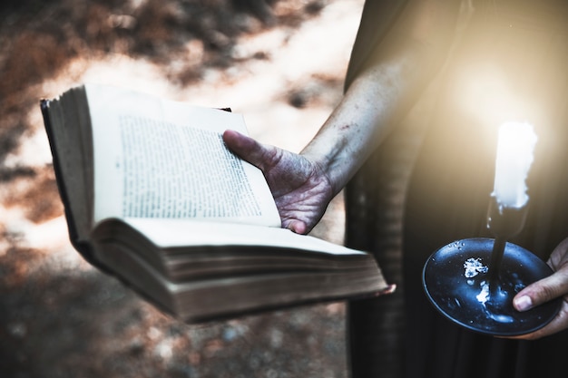 Manos sucias sosteniendo el libro ritual y vela