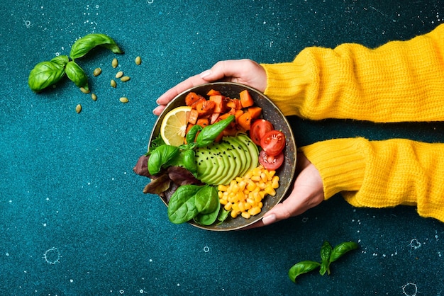 Foto las manos en un suéter amarillo sostienen un cuenco de ensalada calabaza aguacate maíz y tomates concepto de alimentación limpia vista superior