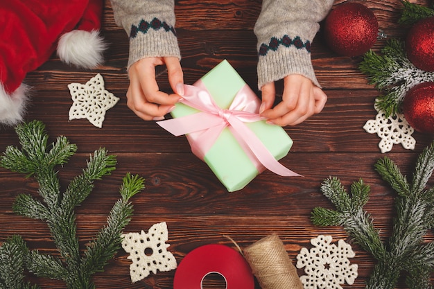 Manos en suéter con un regalo en la mesa de madera con adornos navideños