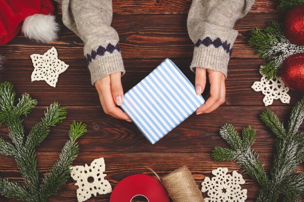 Manos en suéter con un regalo en la mesa de madera con adornos navideños