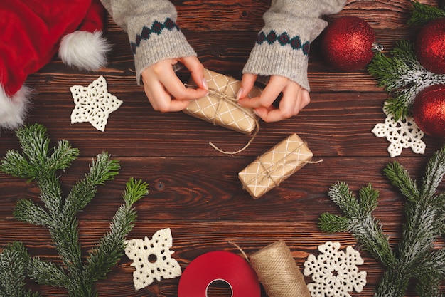 Manos en suéter con un regalo en la mesa de madera con adornos navideños