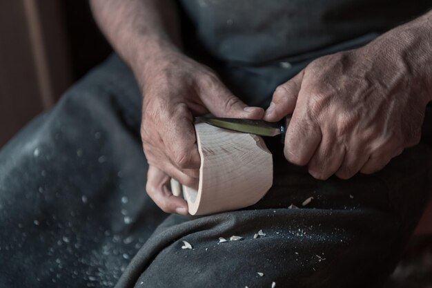 Manos tallando copa de madera, trabajando con cincel de cerca. Taller de madera. Proceso de fabricación de utensilios de cocina de madera Foto de alta calidad.