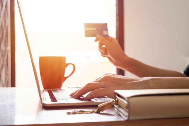 Manos con tarjeta de crédito y usando una computadora portátil Compras en línea