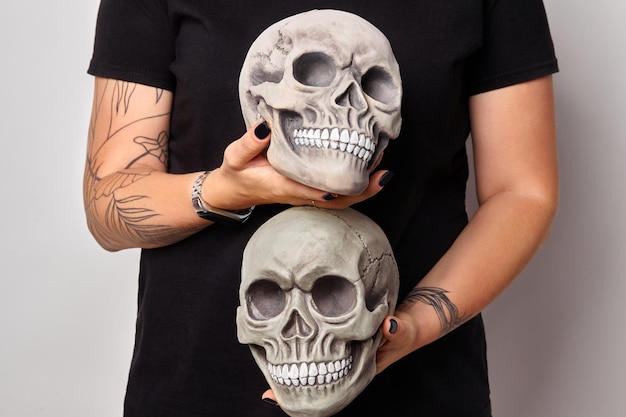 Las manos tatuadas de una mujer con un reloj negro y ropa sostienen un modelo realista de un cráneo humano