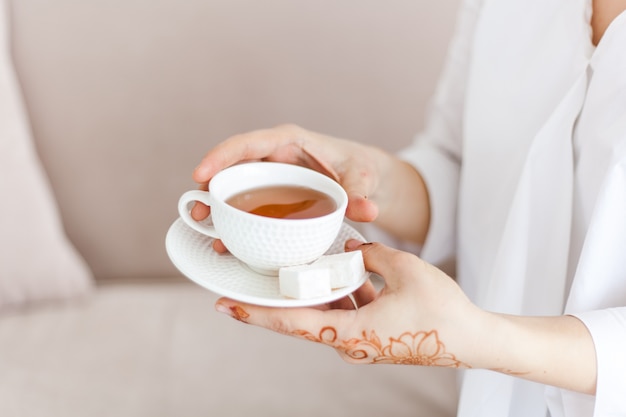 En las manos de una taza de té o café, una bebida en la mañana, almuerzo, manos cubiertas con un patrón tradicional, mahendi, dibujo en las manos.