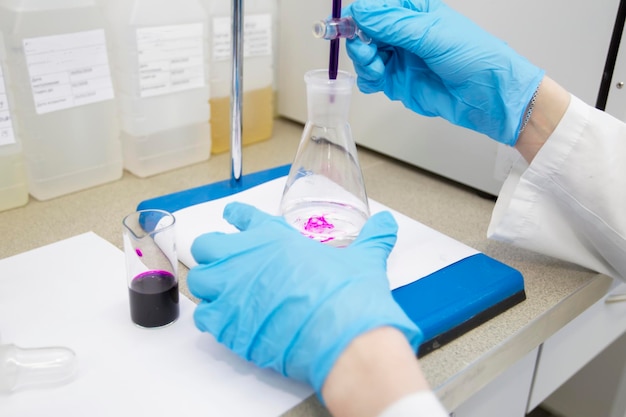 Las manos de un técnico con guantes de goma azules sostienen un matraz