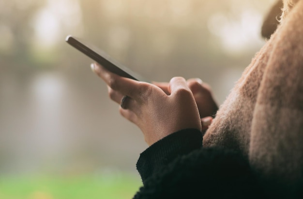 Manos telefónicas y redes sociales con una persona en un fondo borroso al aire libre en un día nublado Contacto móvil y comunicación con un adulto escribiendo un mensaje de texto bajo la lluvia durante el invierno