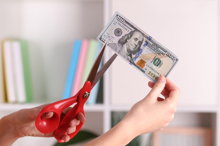 Foto manos con tijeras cortando billetes de dólar en un fondo interior borroso
