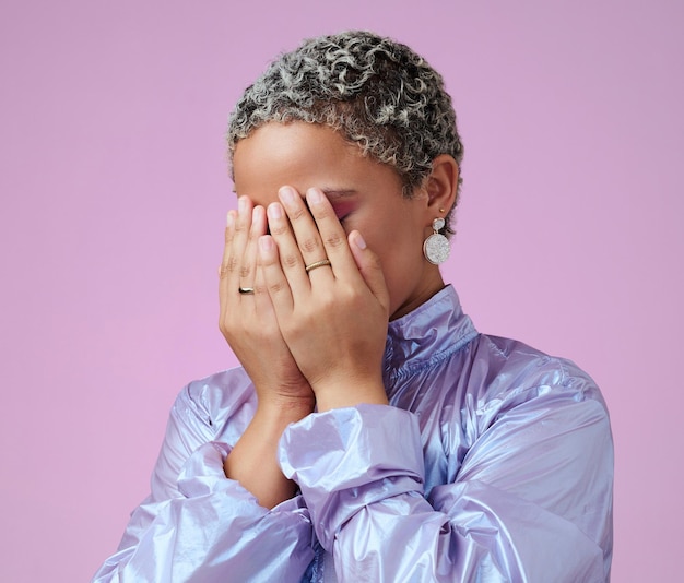 Manos tímidas y escondidas mujer negra en el estudio avergonzada por la moda de moda y el maquillaje vanguardista Belleza cubierta de manos y cara por una linda dama escondida después del glamour y cambio de imagen contra la maqueta de fondo rosa