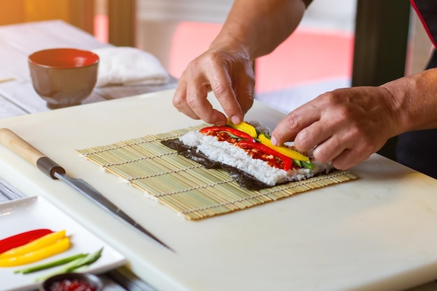 Las manos tocan trozos de pimentón. Pimiento en rodajas sobre arroz. Ingredientes de sushi en estera de bambú. Primera lección en la escuela de cocina.