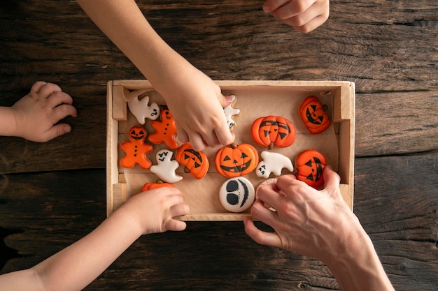 Manos toman galletas Galletas de jengibre de Halloween en caja sobre mesa de madera Divertidas y deliciosas galletas de jengibre para Halloween en la mesa