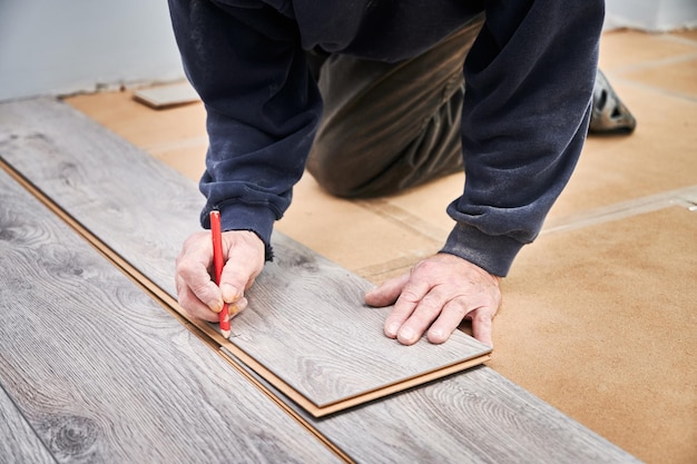 Las manos de un trabajador dibujando una marca en una tabla laminada