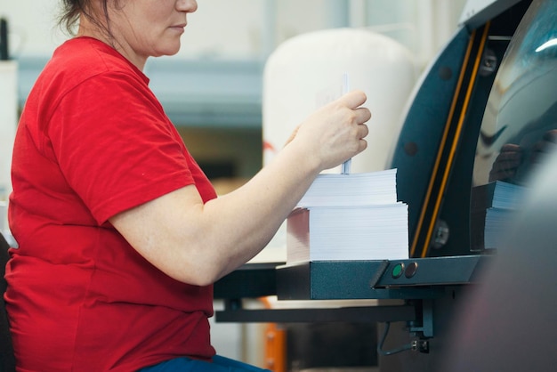 Manos de trabajadora con pilas de papel frente al equipo de maquinaria de impresión