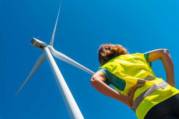 Manos de una trabajadora en una revisión técnica de energía verde de un parque eólico mirando la turbina con un conjunto amarillo