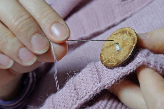 Las manos de las trabajadoras cosen un botón de madera a una chaqueta. de cerca.