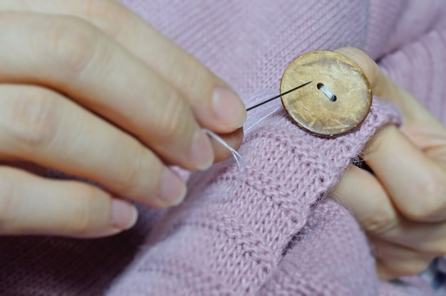 Las manos de las trabajadoras cosen un botón de madera a una chaqueta. de cerca.