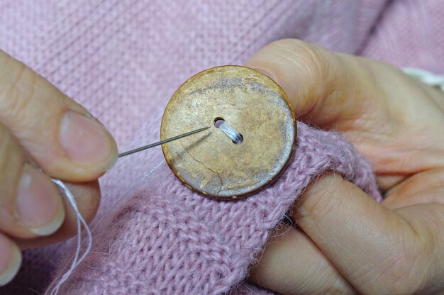 Foto las manos de las trabajadoras cosen un botón de madera a una chaqueta. de cerca.