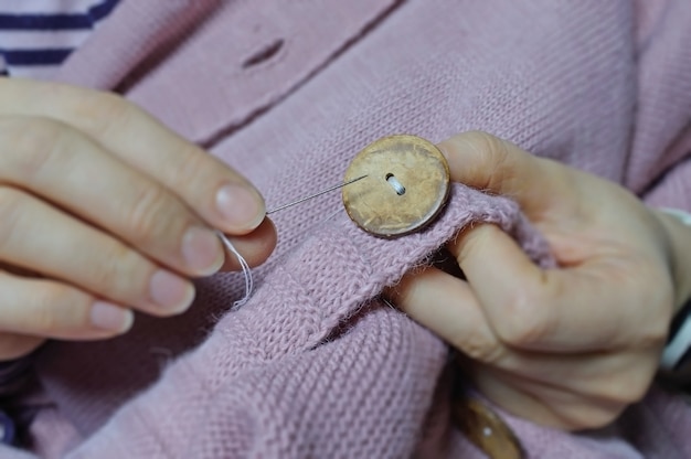 Las manos de las trabajadoras cosen un botón de madera a una chaqueta. de cerca.