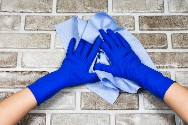 Manos de los trabajadores con guantes protectores de goma con un trapo limpiando la superficie de una mesa o pared en una habitación baño cocina El concepto de limpieza